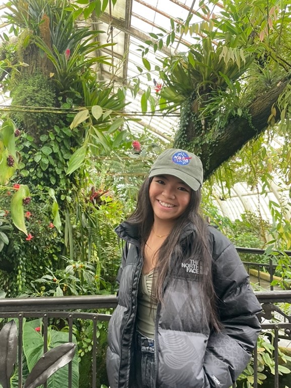 Tiffany wearing a NASA baseball cap in front of greenery.