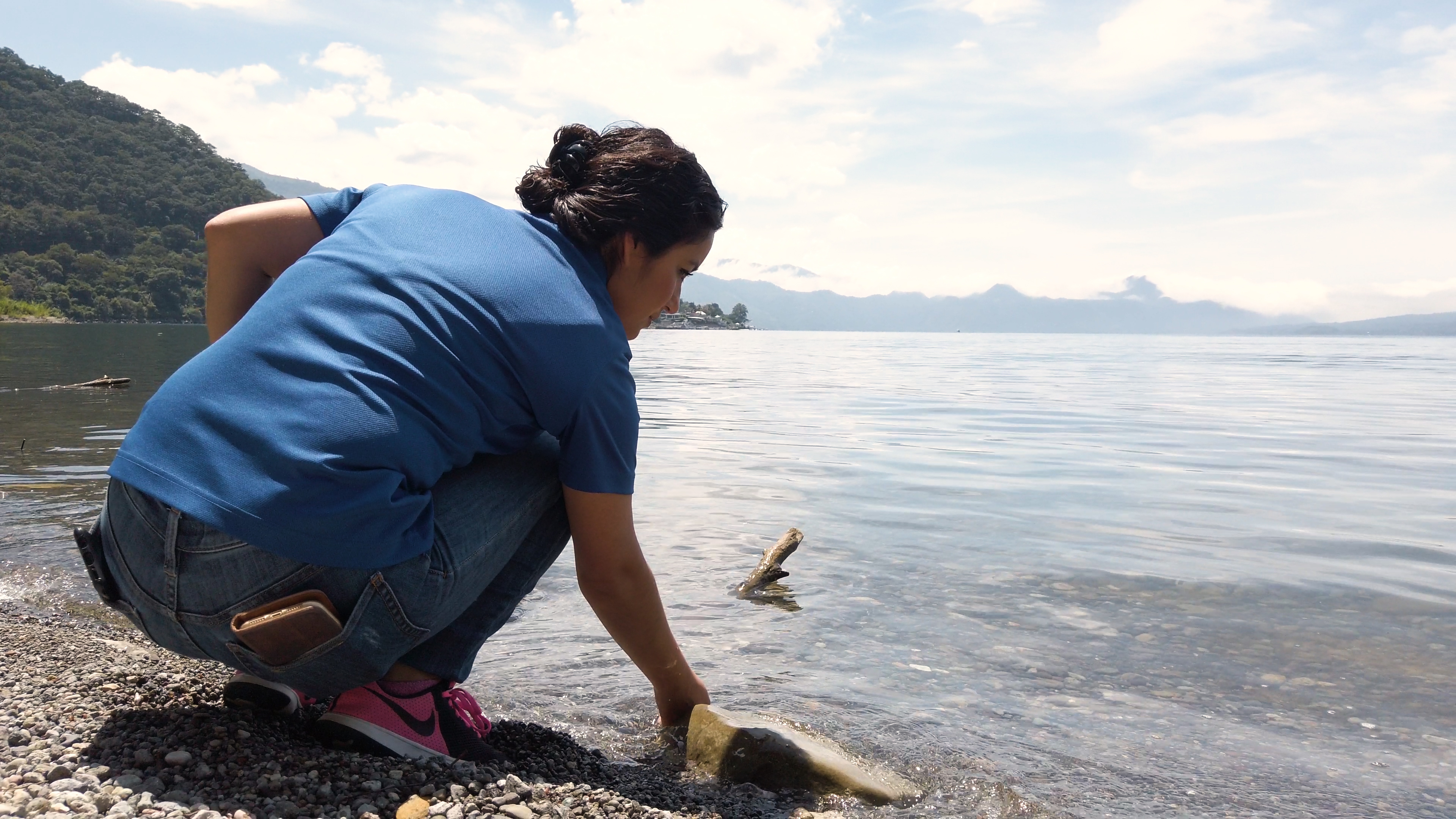 woman on shore reaching hand into water