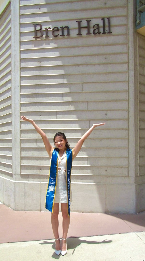 Tiffany celebrating in graduation attire in front of a University building.