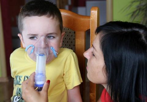 Child being administered an inhaler by woman