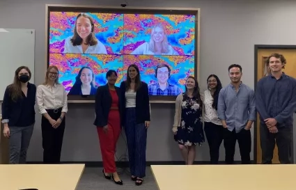 A group of people in a room with others joining virtually on a screen