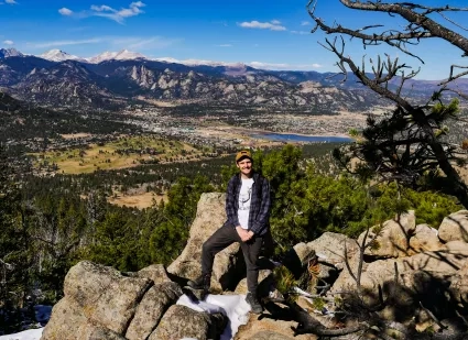 Man in baseball cap stands in front of landscape 