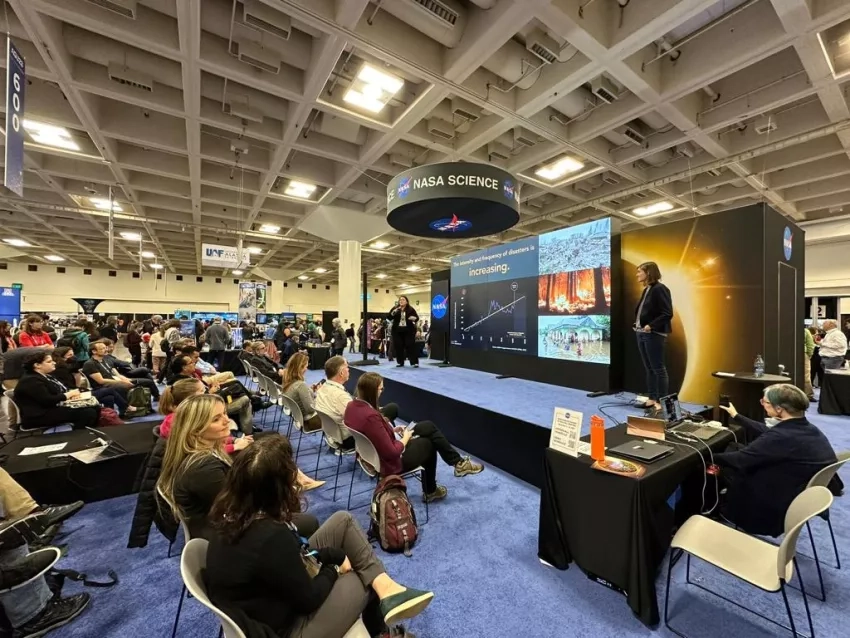 AGU23 attendees watching at Hyperwall Talk - a large dynamic screen on a stage - at the NASA Science Mission Directorate booth. 