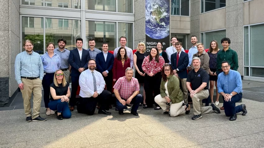 Members of the Disasters Program stand in front of the NASA "Worm" logo at NASA Headquarters in Wasthington, DC.