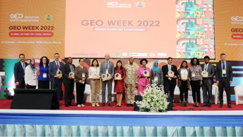 photo of a large group of people standing on a stage, some holding a glass award