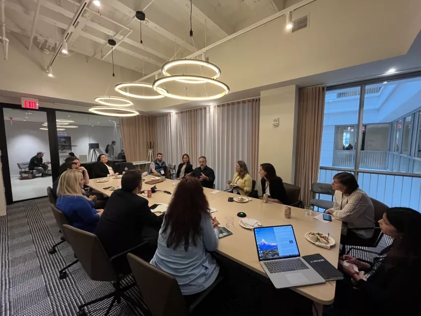 A group of thirteen people eating together at a table while engaged in active discussion to share their knowledge and ideas about building effective partnerships