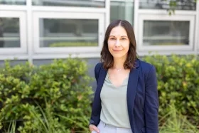 Amber McCullum smiles at the camera, standing in front of greenery and wearing a light green shirt with a navy blue blazer.