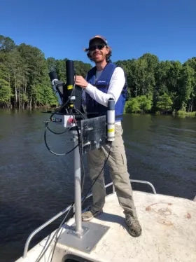 White man in baseball hat installing science instrument on lake