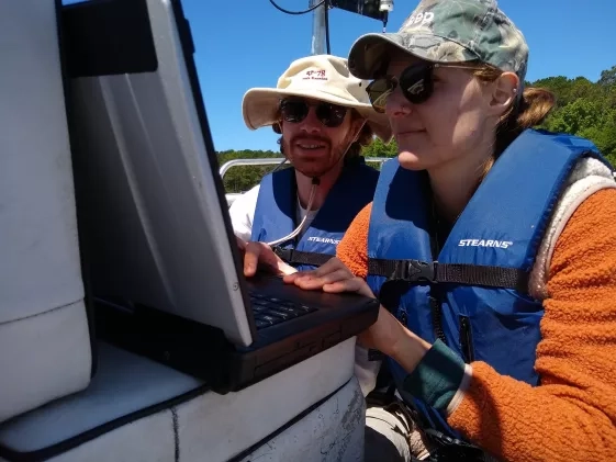 Two white people in baseball caps and sunglasses on a lake