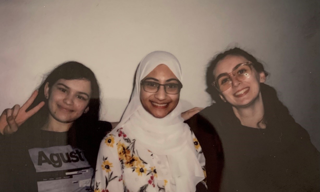 Three women sit together and smile for the camera in a vintage-looking photograph.