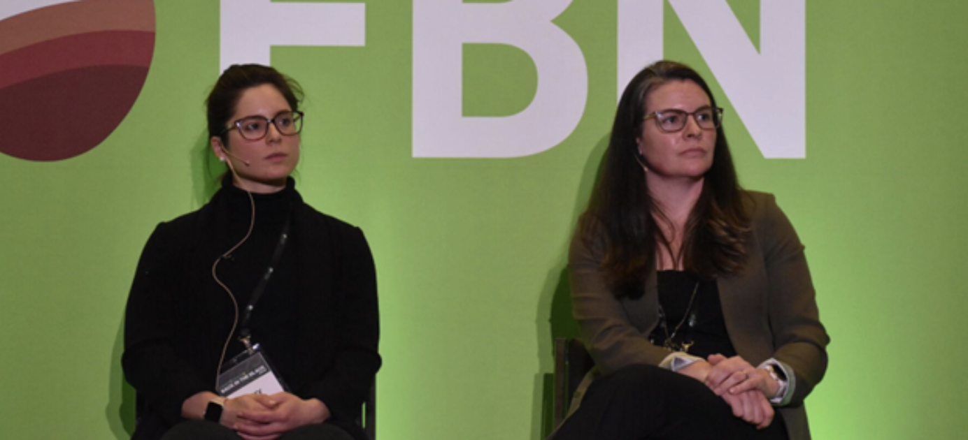 two women seated in front of a green background