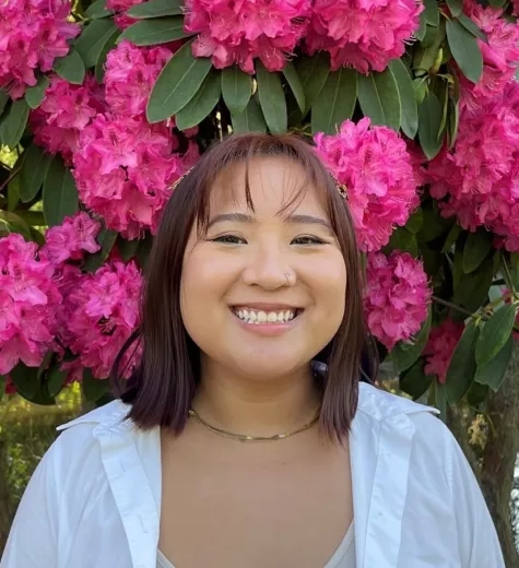 Nati smiles in front of a background of bright pink flowers.