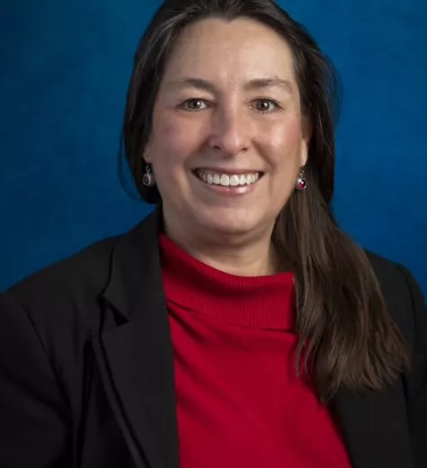 Amber Soja, smiling in front of a blue backdrop, in a red top with a black blazer