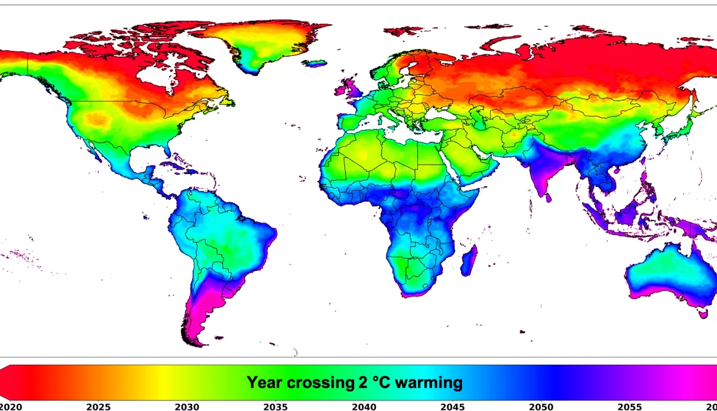 A map uses a rainbow color scheme to depict when areas of the globe are expected to experience 2 degrees celcius of warming. Northern regions are colored red, indicating crossing 2 degrees of warming in 2020, with an irregular gradient to the southern regions shown in purple, indicating 2 degrees of warming by 2060. 