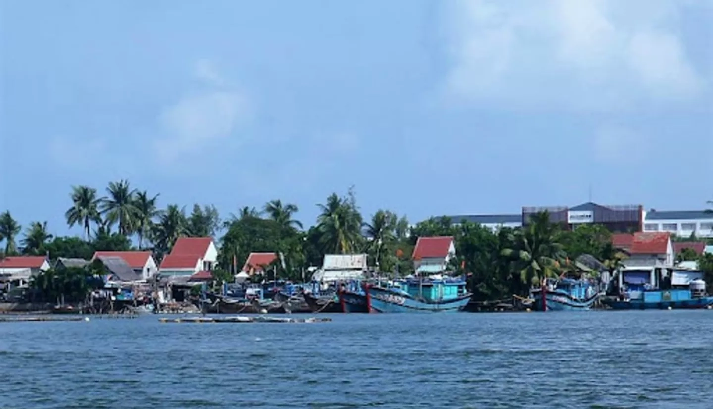 Small building and fishing boats line a palm tree covered riverfront in southern Vietnam