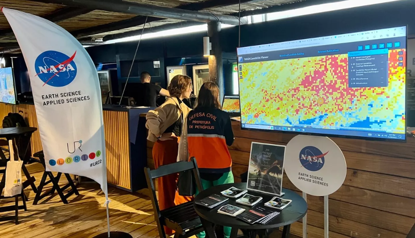 NASA Disasters program science writer Gabriella Lewis speaks with an attendee at the NASA booth.