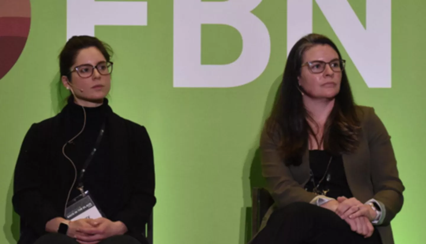 two women seated in front of a green background