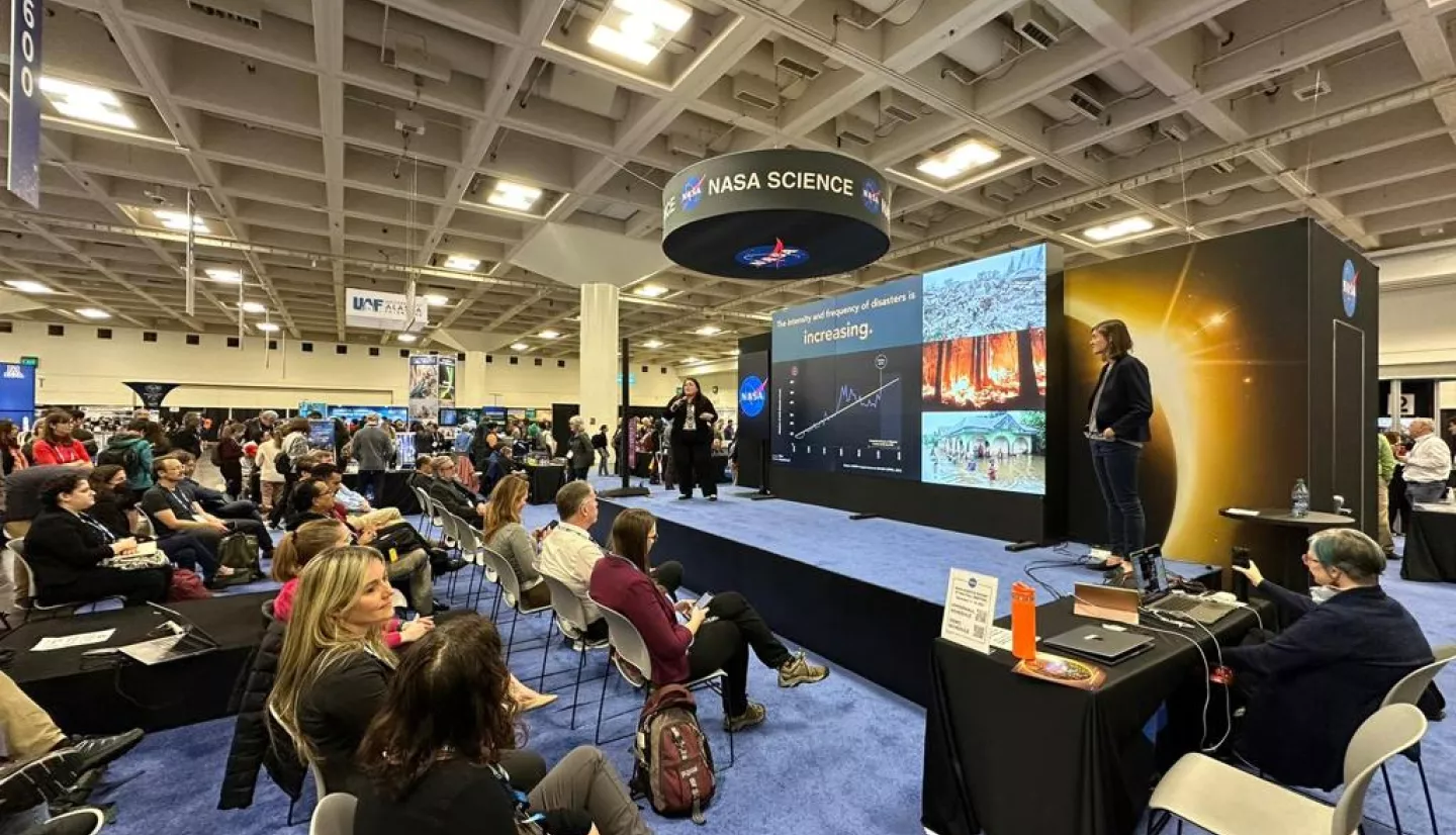 AGU23 attendees watching at Hyperwall Talk - a large dynamic screen on a stage - at the NASA Science Mission Directorate booth. 