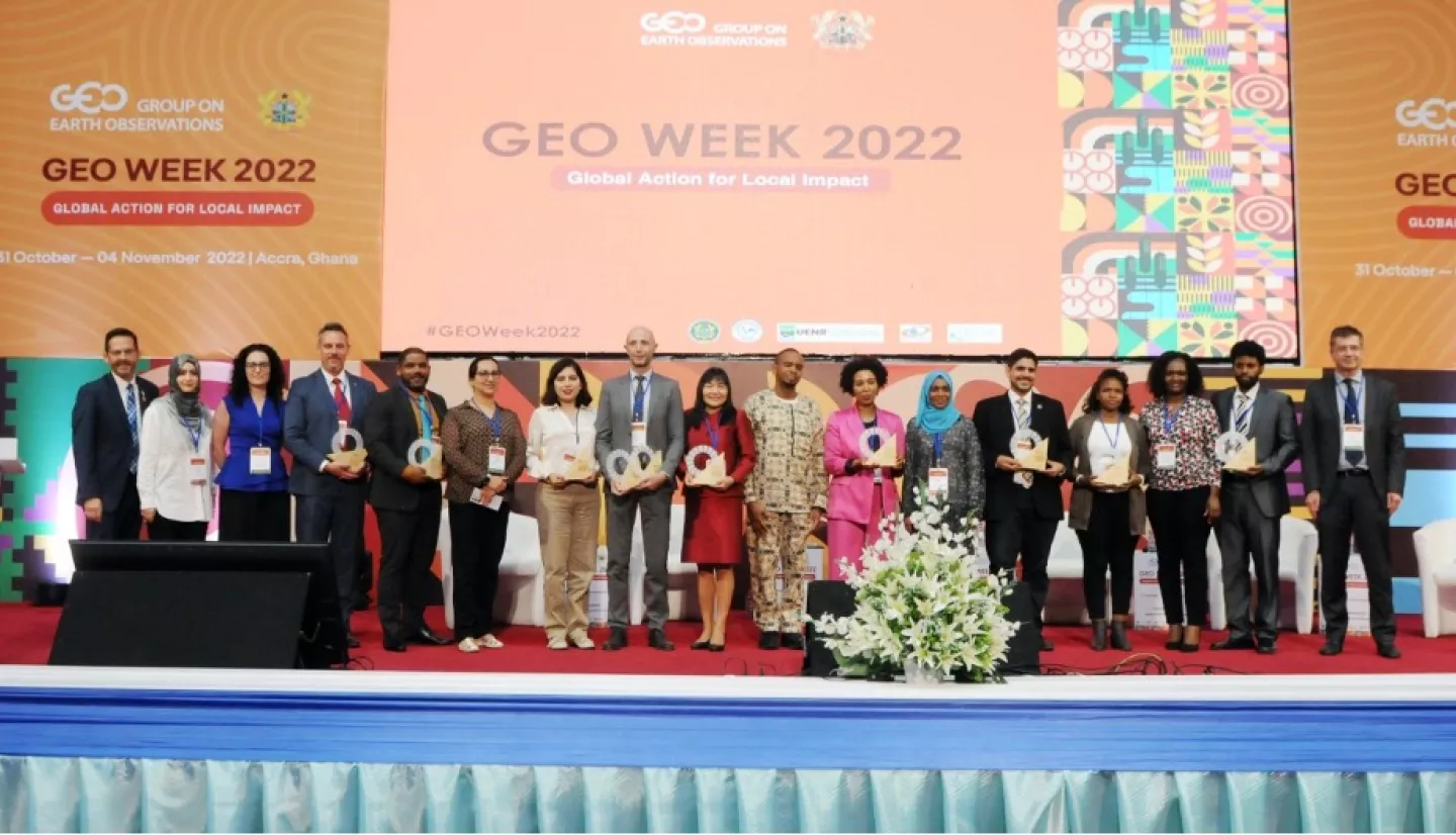 photo of a large group of people standing on a stage, some holding a glass award