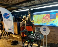 NASA Disasters program science writer Gabriella Lewis speaks with an attendee at the NASA booth.