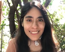 Diana smiles at the camera with greenery behind her.