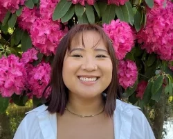 Nati smiles in front of a background of bright pink flowers.