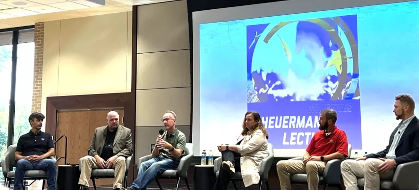 photo of people sitting on a stage talking with a screen behind them says "Heurmann Lecture"